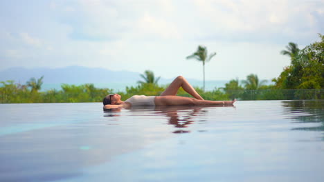 Slim-beautiful-woman-laying-as-if-on-the-water,-sunbathing-with-tropical-landscape-in-the-background-during-bright-sunny-day