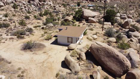 Lonely-small-house-next-to-massive-stone-boulder-in-deadly-desert,-aerial-view