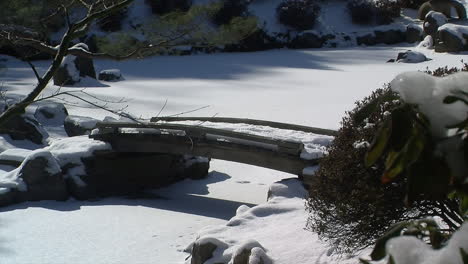 Schneebedeckte-Fußgängerbrücke-überspannt-Im-Winter-Einen-Zugefrorenen-Teich