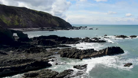 Aerial-shot-of-the-waves-in-the-sea-and-the-rocks-and-hillside-at-Spekes-Mill-coastal-beach-in-Devon