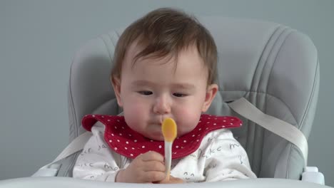 Cute-baby-eating-rice-porridge-meal-from-a-spoon-while-sitting-and-a-baby-chair