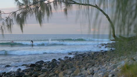 Surfers-Riding-The-Ocean-Waves-And-The-Rocky-Seashore-Of-Little-Cove-Beach-At-Noosa-Heads,-Australia