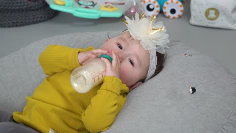 Little-baby-girl-drink-formula-milk-from-a-bottle-and-playing-with-fingers-while-looking-at-camera