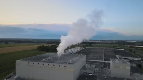Aerial-orbit-of-a-factory-with-steam-rising-from-pipe,-with-beautiful-a-beautiful-sunset-in-the-background