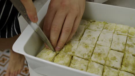 Chef-cuts-Arabic-baklava-into-slices-inside-ceramic-cooking-tray