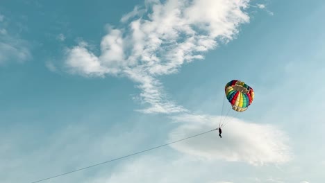 Wide-far-away-slow-motion-shot-of-silhouetted-parasailing-skydiver-with-colourful-parachute