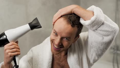 Handsome-curly-man-dries-his-hair-with-a-hair-dryer-in-the-bathroom