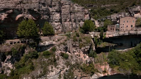 Luftaufnahmen-Eines-Naturraums-In-Einem-Grünen-Tal-Mit-Einem-Gebäude-Und-Einigen-Wasserfällen-In-Katalonien