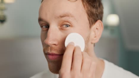 Close-up-portrait-of-a-young-man-wiping-face-with-cotton-pad