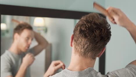 Portrait-in-the-mirror-of-a-young-man-combing-his-hair-with-a-wooden-comb