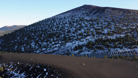 Aerial:-Snow-covered-volcanic-mountain-region-at-Sunset-Crater,-Flagstaff---drone-shot