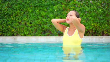 Schöne-Thailändische-Junge-Frau-Im-Pool-Mit-Gelbem-Badeanzug-Streichelt-Nasses-Haar