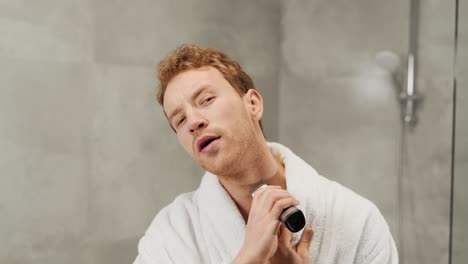 Cute-young-man-shaves-his-beard-with-an-electric-razor