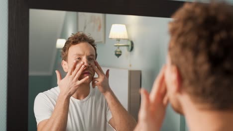 Handsome-man-applying-cream-on-face-in-front-of-a-mirror