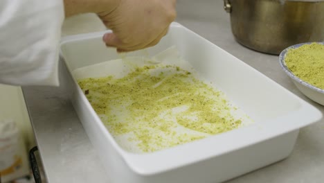 Chef-adds-chopped-nuts-onto-baklava-dough-layer-inside-ceramic-pan