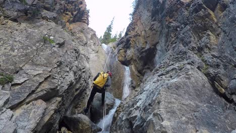 Male-canyoneer-with-pack-rappels-rope-down-river-waterfall-in-canyon