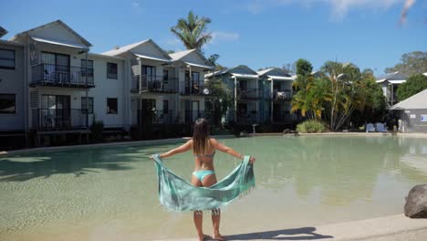 Woman-Poses-At-The-Edge-Of-The-Pool-At-the-Front-Of-Accommodation-Structures-In-Noosa-Lakes-Resort