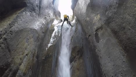 Low-angle-view:-Man-with-yellow-pack-rappelling-river-canyon-waterfall