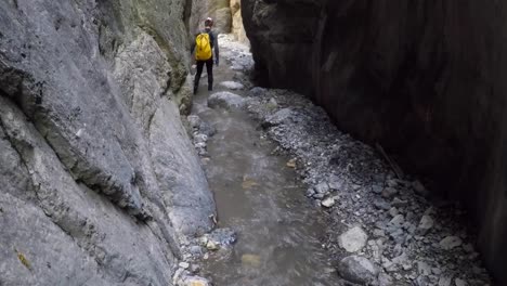 Male-with-yellow-pack-descends-river-canyon-with-flowing-water-on-foot