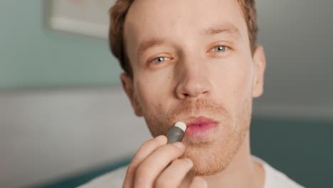 Close-up-portrait-of-a-young-man-using-a-hygienic-lipstick