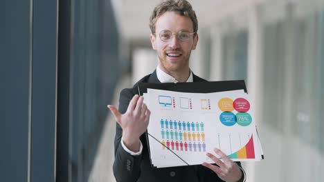 Nice-young-man-holding-slides-with-infographics-giving-a-presentation-looking-at-the-camera