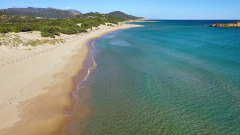 Aerial-tracking-shot-of-beautiful-Su-Giudeu-beach-without-people,-turquoise-water-and-hills-in-the-background-in-South-Sardinia,-Italy