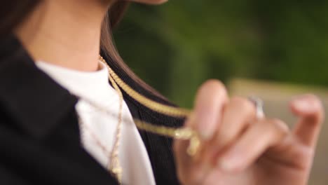close-up-shot-of-a-young-caucasian-woman-touching-her-golden-necklace-jewellery-wearing-silver-rings-stiting-on-a-bench-feeling-nostalgic-relaxing-by-herself-isolated-blurry-backround-slow-motion