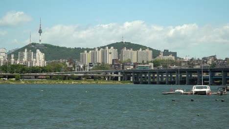 Río-Han,-Torre-Namsan-Y-Puente-Banpo-De-Dos-Pisos-En-El-Fondo,-Catamarán-Y-Bote-Flotando-En-El-Agua