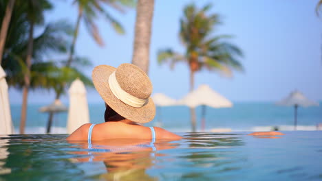 Rücken-Einer-Frau-Im-Swimmingpool-Eines-Tropischen-Hotels-In-Miami,-Verschwommene-Sonnenschirme-Und-Meer-Im-Hintergrund,-Strand-Von-Florida