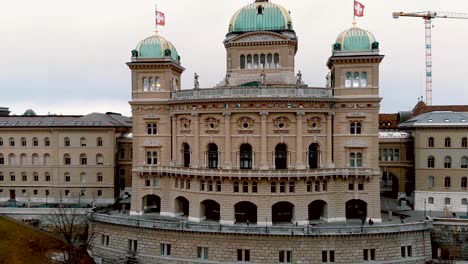 Aerial-establishing-of-Bern-Parliament-Building-with-Swiss-flags-flying