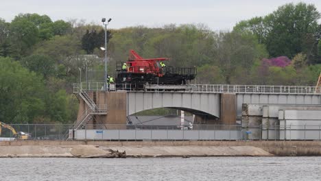 Small-crew-of-men-walking-along-side-a-specialized-crane-moving-on-rails-at-Lock-and-Dam-Number-14-on-the-Mississippi-River,-near-LeClair,-Iowa-USA