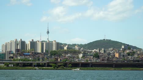 Yacht-Drifting-on-Han-River,-Cars-Traffic-on-Bridge-Namsan-Tower-and-Yongsan-District-villas-and-Apartments-on-Background-on-Sunny-Cloudy-Day,-static