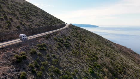 Camper-van,-driving-on-winding-road,-between-mountains-and-sea,-Cres,-Croatia