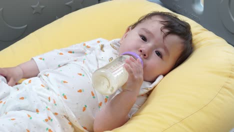 Süßes-Einjähriges-Mädchen,-Das-Eine-Flasche-Milch-Trinkt,-Während-Es-Auf-Einem-Gelben-Kissen-Liegt---Nahaufnahme,-Statische-Aufnahme