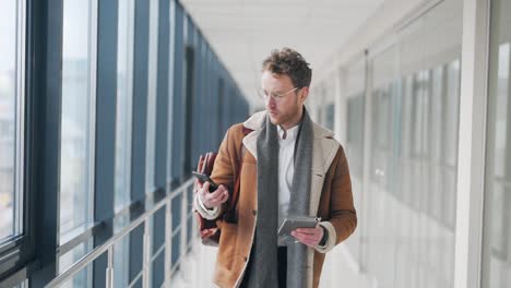 Stylish-adult-man-walking-down-the-hall-receives-a-joyful-letter-on-a-smartphone