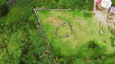 Aerial-top-down-showing-circle-of-people-doing-morning-sport-outdoors-in-garden-at-beach