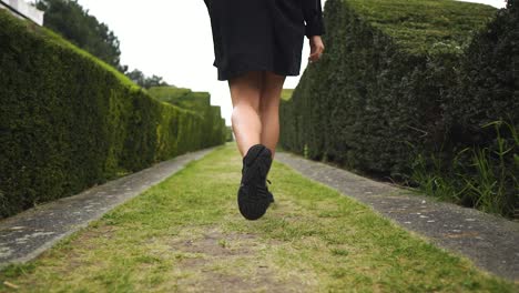 beautiful-model-has-a-great-body-walking-in-green-maze-with-her-jacket-open-looking-at-her-hand-following-footpath-slow-motion-cloudy-settings
