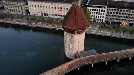 Aerial-view-of-Kapellbrücke-bridge-in-Lucerne,-Switzerland-spinning-around-the-bridge-tower-to-reveal-the-historical-Altstadt