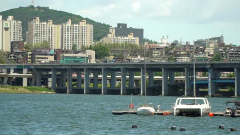 Barcos-Flotando-En-El-Río-Han-En-Seúl,-Corea-Del-Sur-Con-El-Puente-Banpo-Y-El-Horizonte-De-La-Ciudad-En-Segundo-Plano