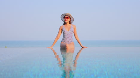 Gorgeous-Asian-woman-sitting-on-infinity-pool-border-leaning-on-hands-and-looking-around-slow-motion-static-copy-space-template