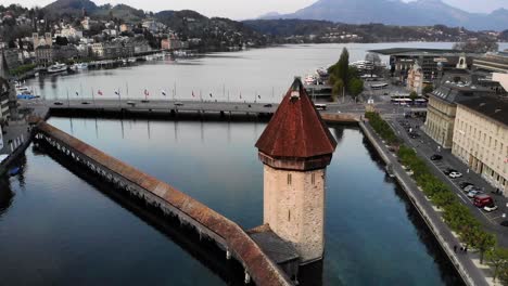 Aerial-view-of-Lucerne,-Switzerland-while-flying-alongside-Kapellbrücke-bridge-with-a-view-of-the-lake-at-dusk