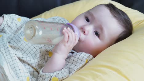 Close-up-Of-An-Adorable-Baby-Girl-Drinking-Her-Milk-While-Resting-On-A-Yellow-Pillow---static-shot