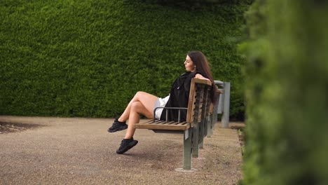 unique-instagram-dancer-influencer-revealing-shot-sitting-on-bench-raising-her-leg-stretching-waiting-for-her-date-alone-in-green-maze-sad-dissapointed-impatient-cloudy-slow-motion-concrete-ground