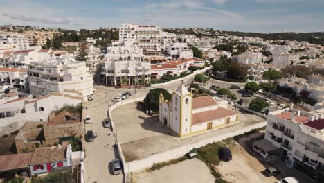 Church-of-Nossa-Senhora-da-Luz-surrounded-by-townscape,-Algarve---Aerial