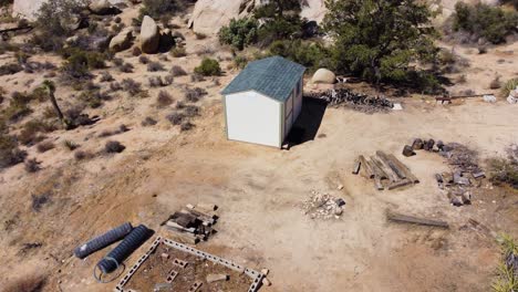Tiny-shed-surrounded-by-desert-and-huge-boulders-in-aerial-orbit-view