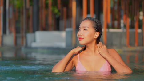Portrait-of-Asian-Woman-Gently-Squeezing-Wet-Hair-and-touching-the-tanned-body-in-swimming-pool-of-a-luxury-hotel-in-Bora-Bora