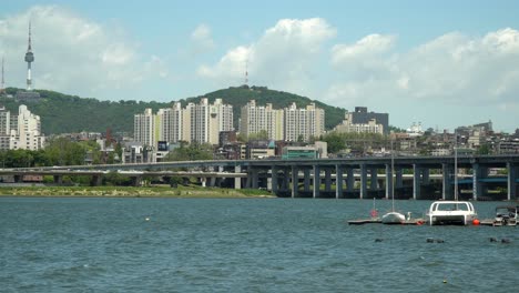 Han-river-near-Banpo-bridge,-Catamaran-and-sailing-boat-floating-in-dock-Namsan-Seoul-Tower-on-Background-on-cloudy-sunny-day-no-dust,-wide-angle,-static