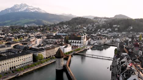 Aerial-view-of-Lucerne,-Switzerland-with-a-view-of-Mount-Pilatus-in-the-background-while-moving-over-Kapellbrücke-bridge-towards-the-Jesuit-Church
