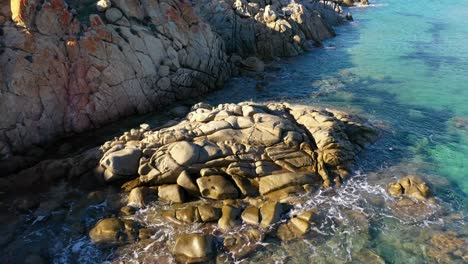 Aerial-shot-of-rocks-in-clear-turquoise-water-in-front-of-Su-Giudeu-beach-in-South-Sardinia,-Italy