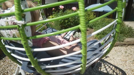 Woman-reads-eBook-novel-relaxing-in-comfortable-garden-hammock-on-hot-sunny-day